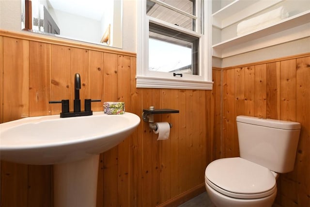 bathroom featuring sink, toilet, and wood walls