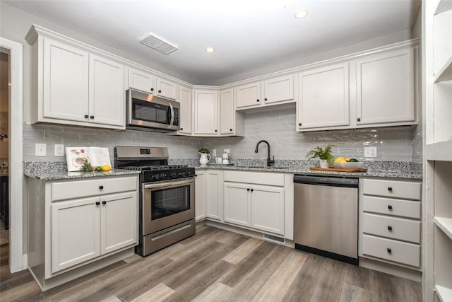 kitchen with white cabinets, appliances with stainless steel finishes, light stone counters, and hardwood / wood-style floors