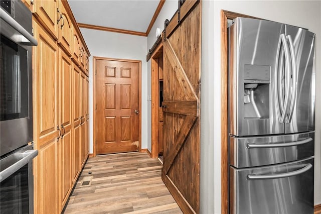 kitchen with stainless steel appliances, crown molding, a barn door, and light hardwood / wood-style floors