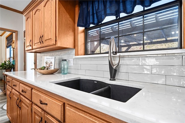 kitchen featuring wood-type flooring, tasteful backsplash, sink, ornamental molding, and light stone counters