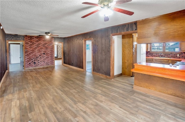 unfurnished living room with sink, brick wall, wood walls, a textured ceiling, and light wood-type flooring