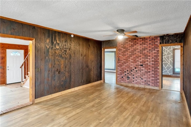 spare room featuring light wood-type flooring, brick wall, a textured ceiling, ceiling fan, and wood walls