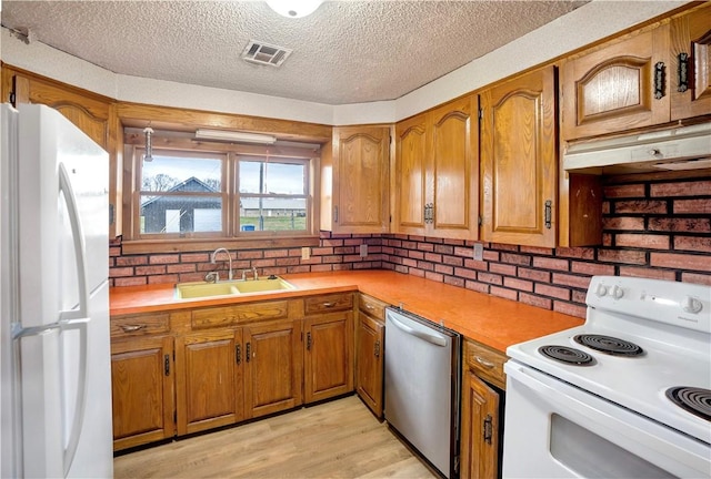 kitchen with light wood-type flooring, a textured ceiling, white appliances, and sink