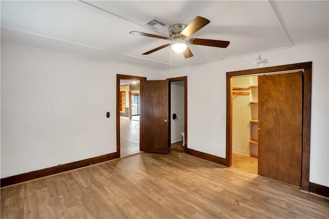 unfurnished bedroom featuring ensuite bath, ceiling fan, a walk in closet, a closet, and light wood-type flooring