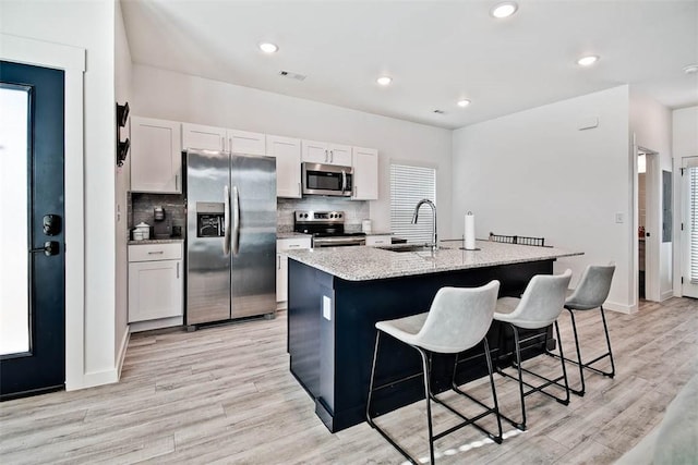 kitchen with a kitchen bar, stainless steel appliances, a kitchen island with sink, sink, and white cabinetry