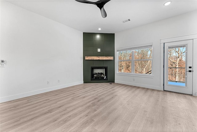 unfurnished living room with a large fireplace, light hardwood / wood-style floors, and ceiling fan