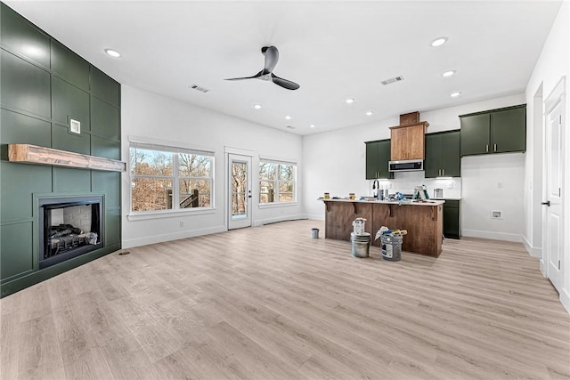 kitchen featuring a fireplace, light hardwood / wood-style flooring, a kitchen island with sink, and ceiling fan