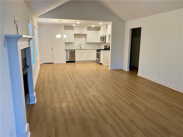 unfurnished living room with sink, light hardwood / wood-style floors, lofted ceiling, and a notable chandelier