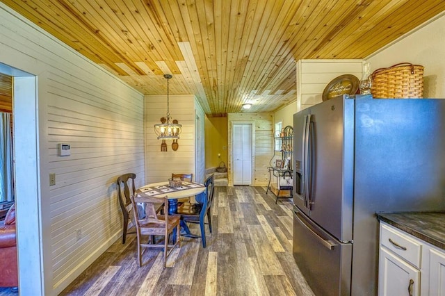 dining area featuring dark wood-type flooring, wooden ceiling, a chandelier, and wood walls