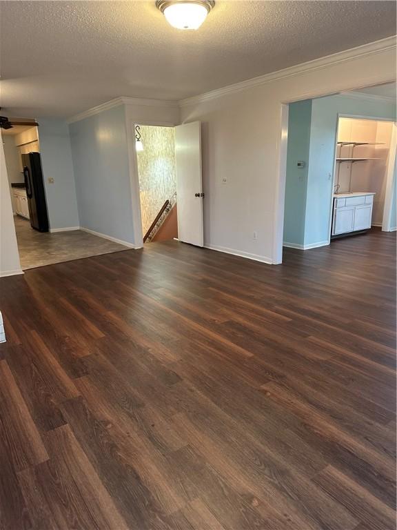 spare room with a textured ceiling, baseboards, dark wood finished floors, and crown molding