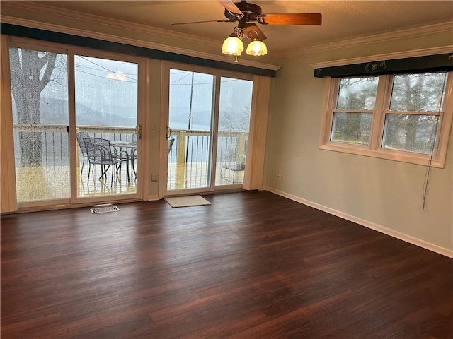 empty room with dark wood-style floors, ornamental molding, baseboards, and a healthy amount of sunlight