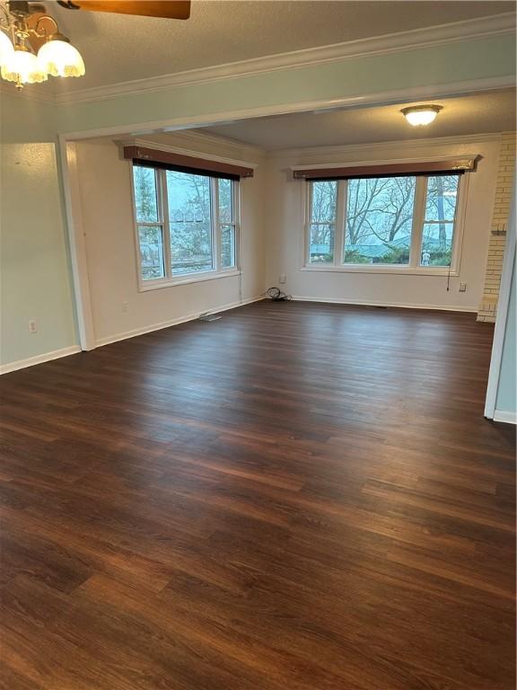 spare room with dark wood finished floors, crown molding, baseboards, and an inviting chandelier