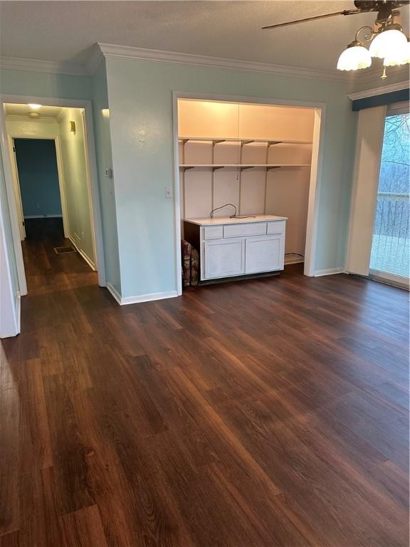 unfurnished living room featuring baseboards, dark wood-type flooring, and crown molding