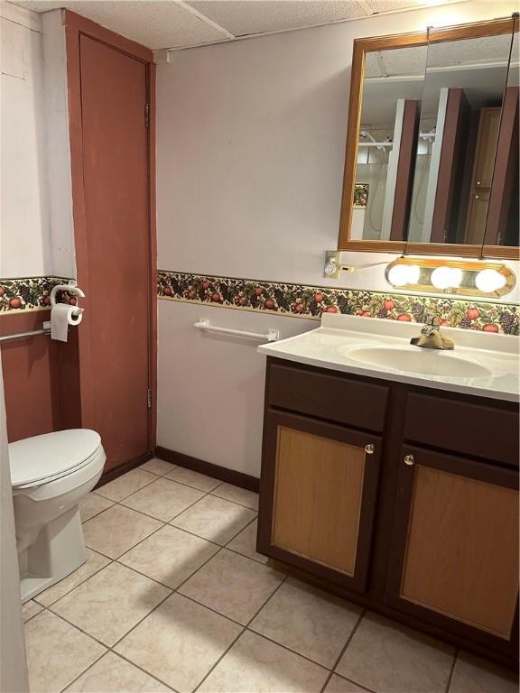 bathroom with toilet, a paneled ceiling, tile patterned flooring, and vanity