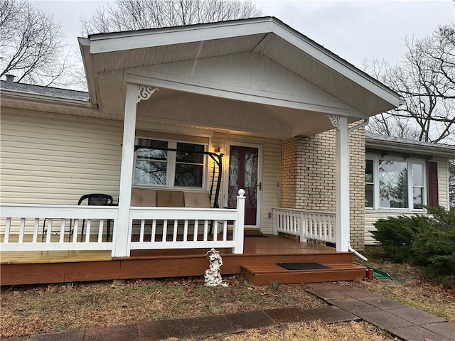 view of exterior entry with a porch and brick siding