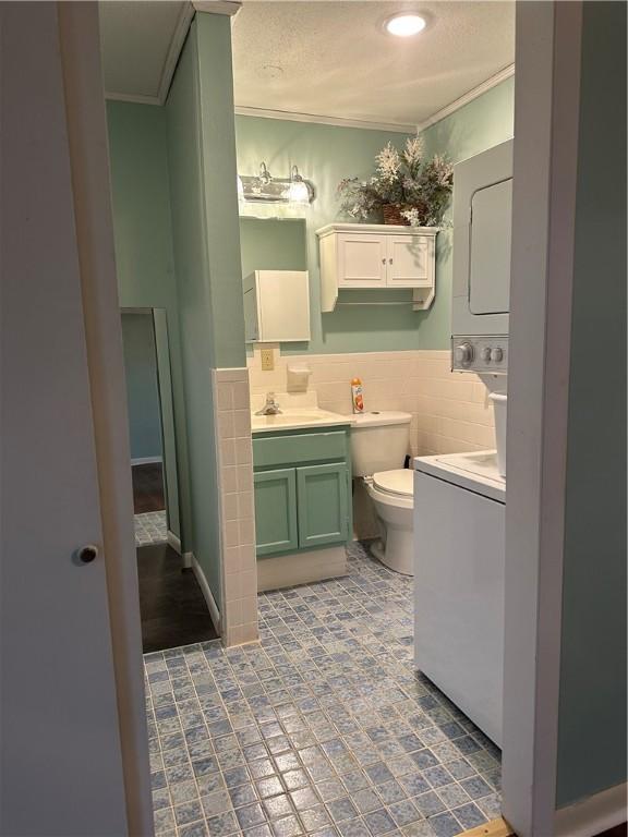 bathroom featuring toilet, ornamental molding, vanity, and tile walls