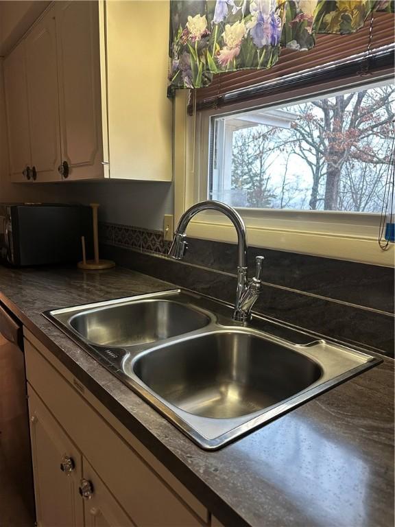 kitchen featuring stainless steel dishwasher, dark countertops, a sink, and white cabinetry