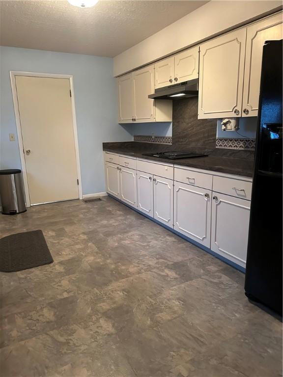 kitchen with a textured ceiling, under cabinet range hood, decorative backsplash, black appliances, and dark countertops