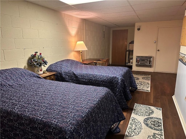 bedroom with concrete block wall, a wall unit AC, a drop ceiling, and wood finished floors