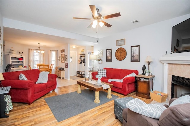 living room featuring a tiled fireplace, light hardwood / wood-style floors, and ceiling fan with notable chandelier