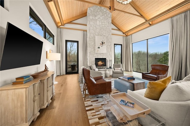 living room featuring high vaulted ceiling, a stone fireplace, light wood-type flooring, beamed ceiling, and wood ceiling