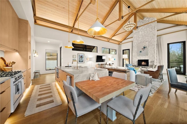 dining space with sink, a stone fireplace, beamed ceiling, high vaulted ceiling, and wood ceiling