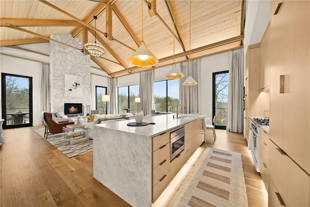 kitchen featuring pendant lighting, a kitchen island with sink, high vaulted ceiling, a fireplace, and beamed ceiling