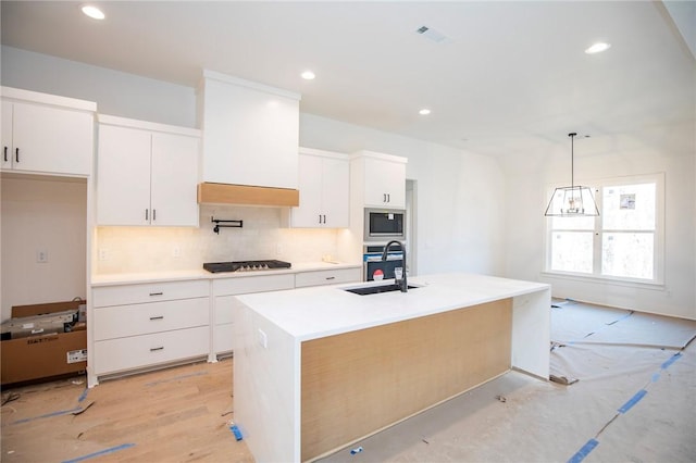 kitchen with light countertops, backsplash, appliances with stainless steel finishes, white cabinets, and a sink