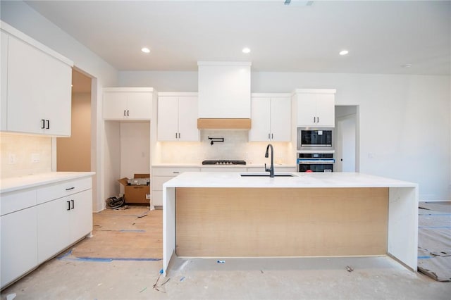 kitchen featuring a center island with sink, white cabinets, stainless steel appliances, premium range hood, and a sink