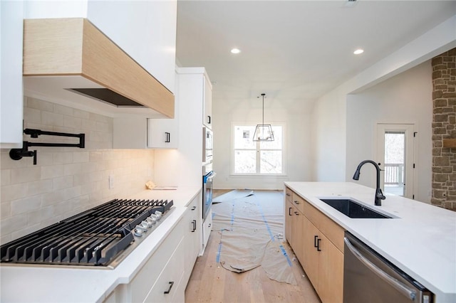 kitchen featuring tasteful backsplash, light countertops, light wood-style flooring, appliances with stainless steel finishes, and a sink