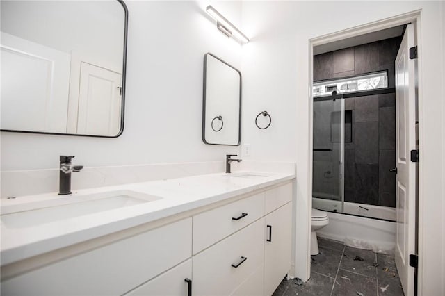 bathroom with double vanity, bath / shower combo with glass door, a sink, and toilet