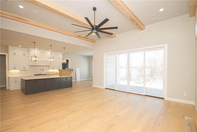 kitchen with beam ceiling, ceiling fan, a spacious island, decorative light fixtures, and white cabinets