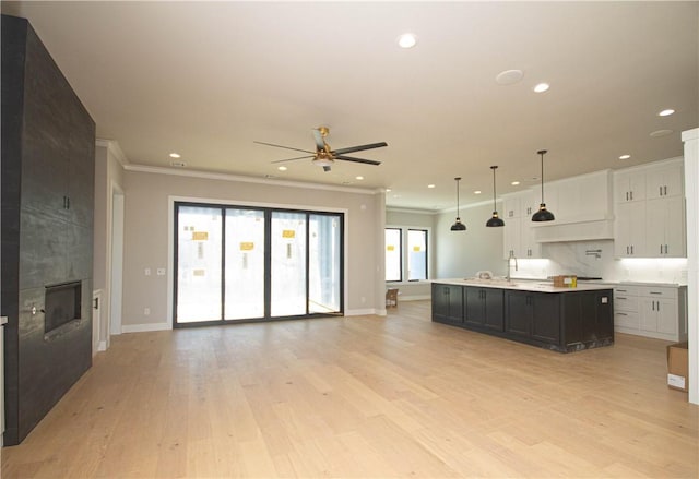 kitchen featuring pendant lighting, light hardwood / wood-style floors, white cabinetry, a large island, and a tiled fireplace