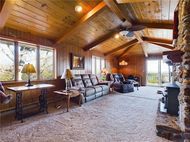 living room with wood walls, ceiling fan, carpet, a wood stove, and vaulted ceiling with beams