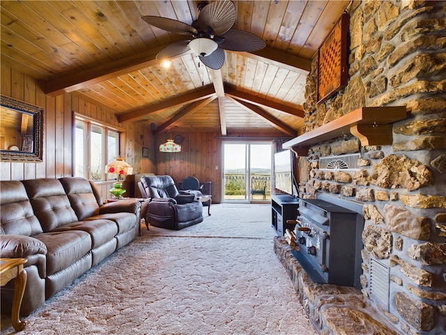 carpeted living room featuring ceiling fan, vaulted ceiling with beams, wood walls, and a wood stove