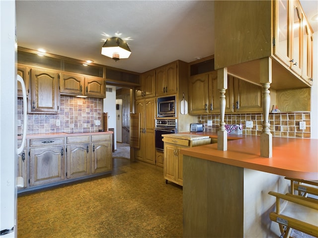 kitchen featuring stainless steel microwave, backsplash, oven, a kitchen bar, and kitchen peninsula