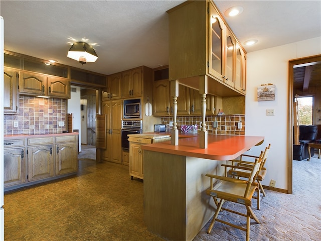 kitchen featuring tasteful backsplash, oven, a breakfast bar, kitchen peninsula, and built in microwave