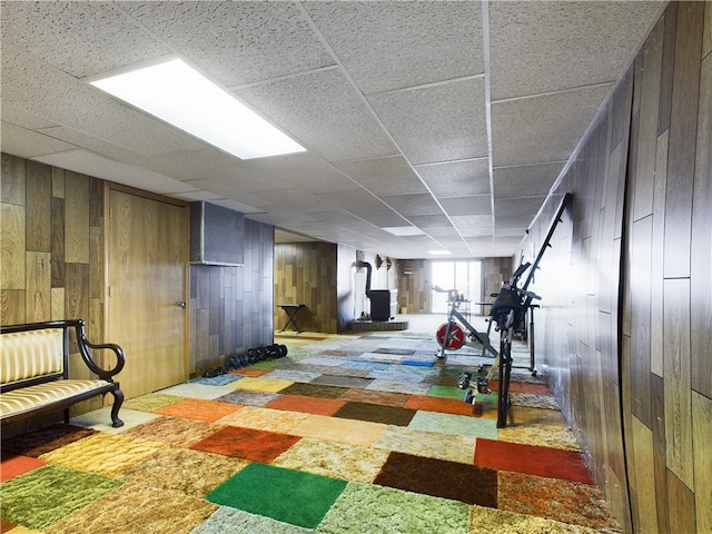 basement with carpet, a drop ceiling, wood walls, and a wood stove