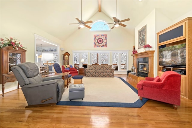 living room with a tiled fireplace, ceiling fan, high vaulted ceiling, and light hardwood / wood-style floors