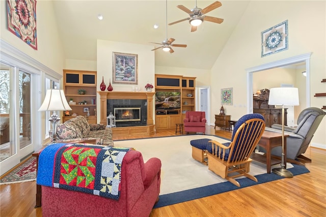 living room with ceiling fan, wood-type flooring, built in features, and high vaulted ceiling