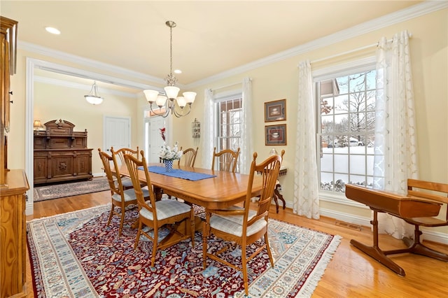 dining area with crown molding, a chandelier, and light wood-type flooring