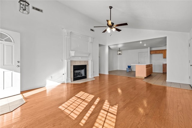 unfurnished living room featuring a tile fireplace, lofted ceiling, ceiling fan with notable chandelier, and light wood-type flooring