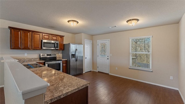 kitchen featuring kitchen peninsula, sink, dark wood-type flooring, appliances with stainless steel finishes, and a textured ceiling