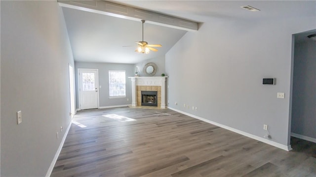 unfurnished living room featuring ceiling fan, dark hardwood / wood-style flooring, a tile fireplace, and lofted ceiling with beams