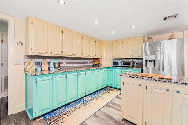 kitchen with backsplash, stainless steel fridge with ice dispenser, light stone counters, and light wood-type flooring