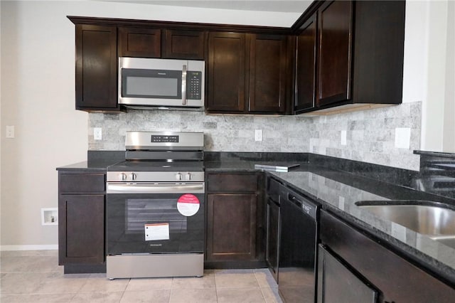 kitchen featuring dark brown cabinetry, dark stone countertops, stainless steel appliances, and light tile patterned flooring