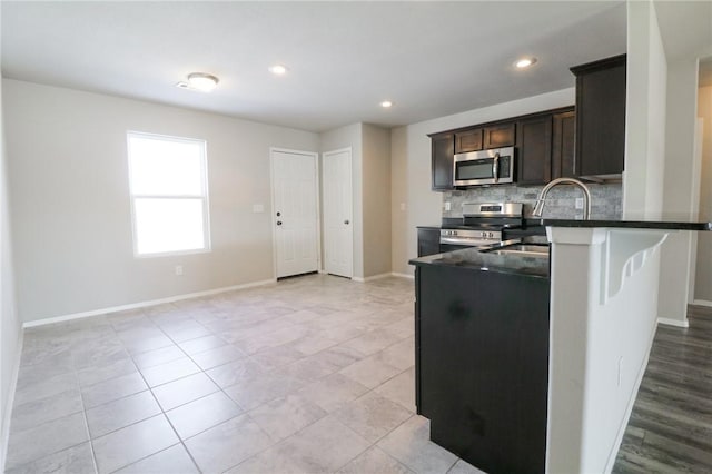 kitchen with appliances with stainless steel finishes, tasteful backsplash, sink, kitchen peninsula, and dark brown cabinets