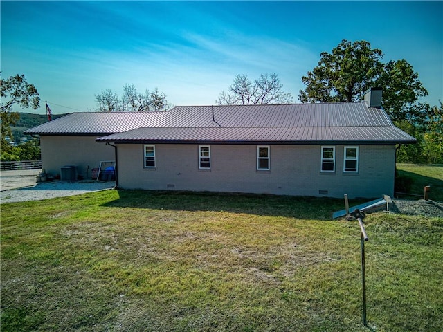 back of house featuring a chimney, metal roof, crawl space, a yard, and brick siding