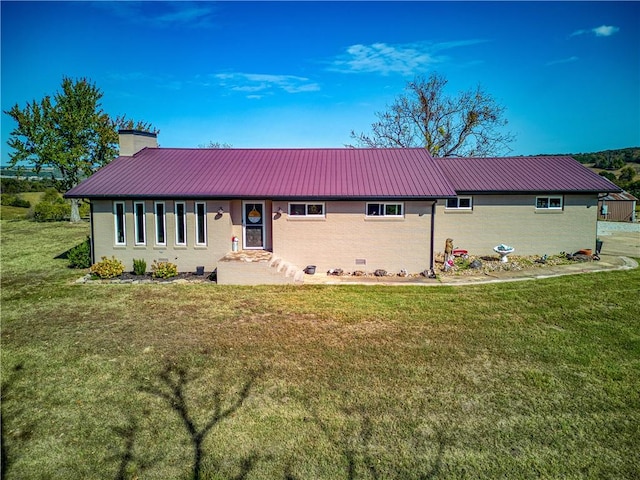 back of property with metal roof, a yard, crawl space, and a chimney