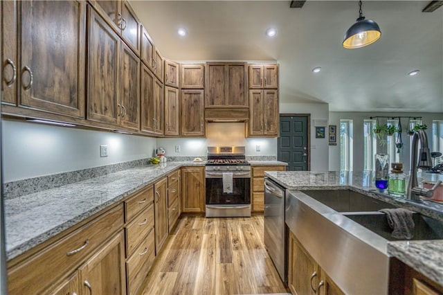 kitchen featuring appliances with stainless steel finishes, brown cabinets, light stone counters, under cabinet range hood, and pendant lighting